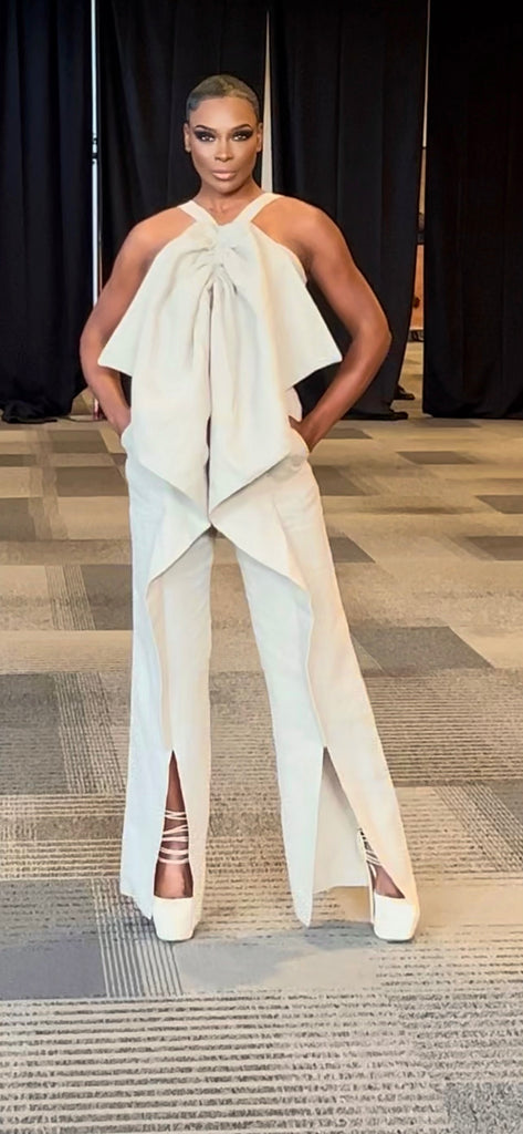 A lady is wearing a linen jumpsuit that has spaghetti straps and a large bow that trails down both pant legs
